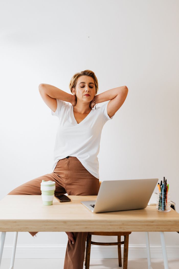 A woman in modern office setup takes a stretch break, embodying relaxed workplace culture.