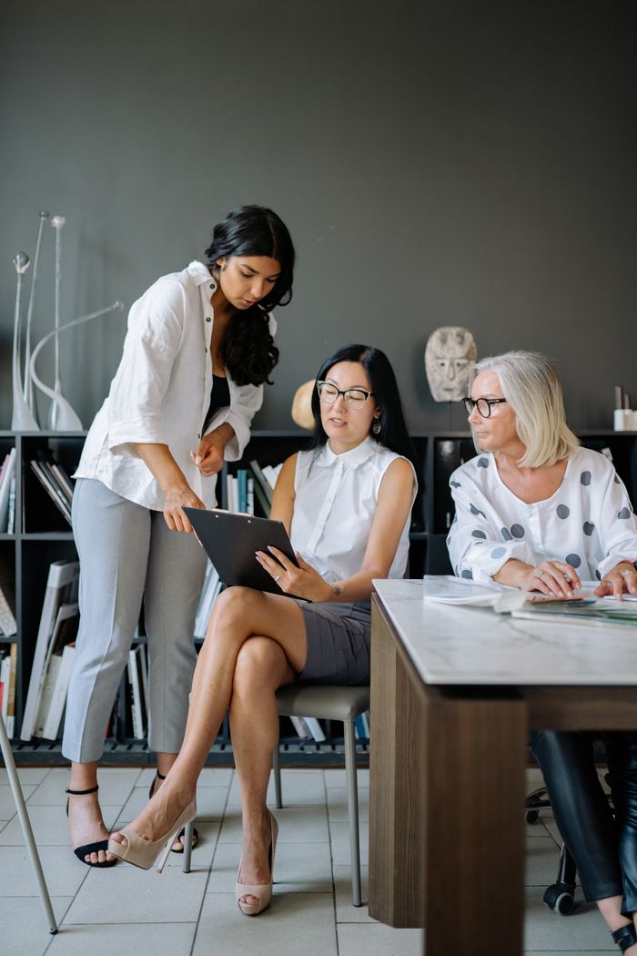 Three professional women engaged in a collaborative discussion in a modern office environment.